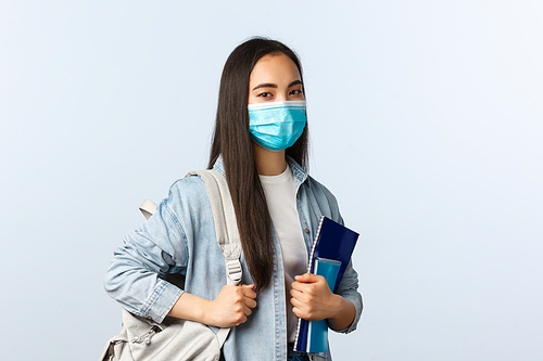 Covid-19 pandemic, education during coronavirus, back to school concept. Stylish modern asian female student at college, carry backpack and notebooks studying material, look camera.