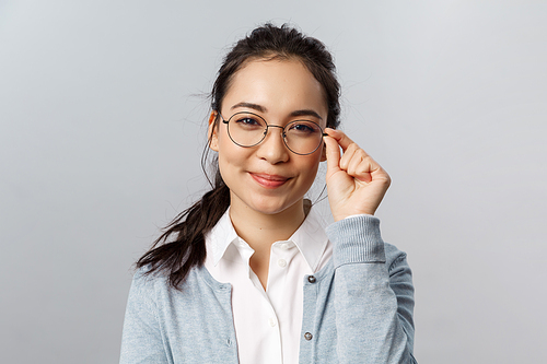 Advertisement, people and emotion concept. Close-up portrait of smart and creative young asian female teacher, office employee, fixing glasses on face and smiling pleased, look determined like pro.