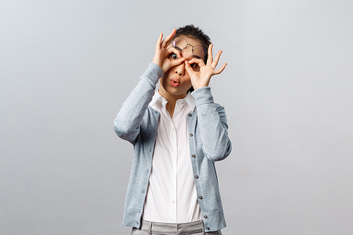 Lifestyle, people and emotions concept. Funny, playful silly asian girl fool around, playing with you, make glasses mask with fingers over eyse, peekabo at kid, staring camera joyful.