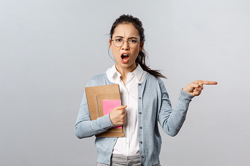 Education, teachers, university and schools concept. Angry and displeased strict tutor, teacher scolding student and tell leave class now, pointing at door shouting annoyed, grey background.