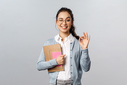 Education, teachers, university and schools concept. Girl guarantee you will like this language courses. Cheerful smiling asian woman show okay sign and wink, recommend study her, hold notebooks.