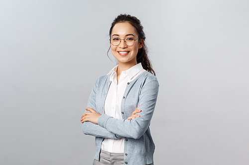 Education, women and lifestyle concept. Attractive asian female entrepreneur, girl tutor smiling satisfied, cross hands chest, pleased help customer with any question, grey background.