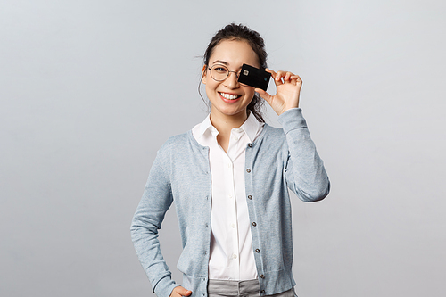 Technology, online purchases and finance concept. Good-looking, lovely asian woman in glasses, showing credit card over eye and smiling, recommend pay internet with bank account.