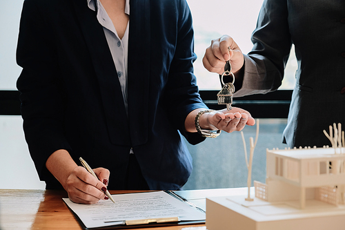 estate agent giving house keys to man and sign agreement in office.