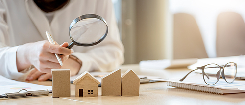 Looking for real estate agency, property insurance, mortgage loan or new house. Woman with magnifying glass over a wooden house at her office.