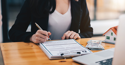 close-up view hands of businesswoman signing leasing home documents and house model on wooden desk.