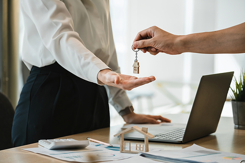 close up view hand of property realtor landlord giving a key house to buyer tenant at modern office.