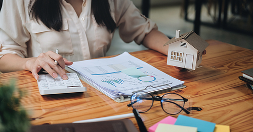 businesswoman with house model doing finances and calculate about cost to real estate investment and in other, tax system. Business Financing Accounting Banking Concept,