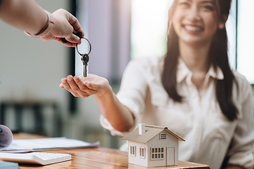 close up view hand of property realtor landlord giving a key house to buyer tenant at modern office