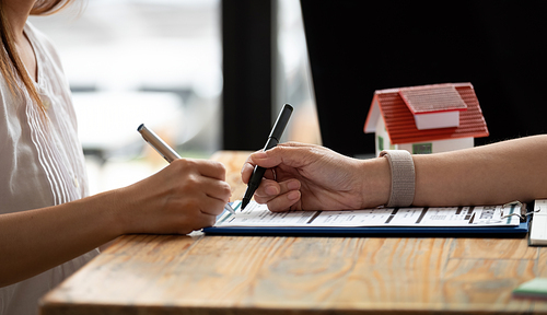 close up view hands of businessman signing leasing home documents and have a apartment keys on paperwork.