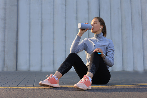 Young female runner is having break, drinking water during the run outdoor in city.