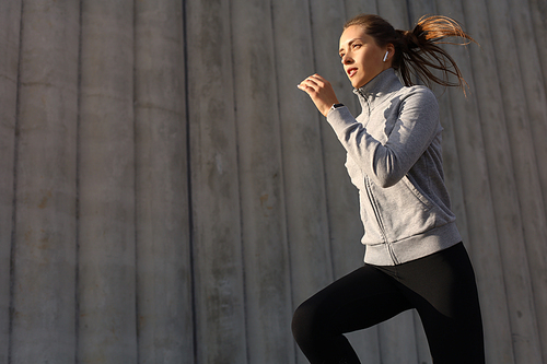 Young attractive sporty fitness woman running while exercising outdoors at sunset or sunrise in city.