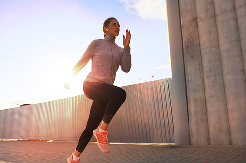 Young attractive sporty fitness woman running while exercising outdoors at sunset or sunrise in city.