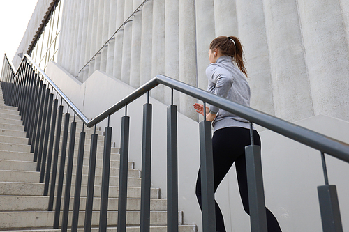 Rear view of runner athlete running on stairs. Woman fitness is jogging oudoors.