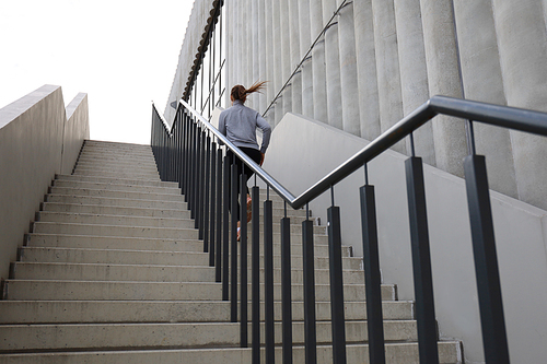 Rear view of runner athlete running on stairs. Woman fitness is jogging oudoors.