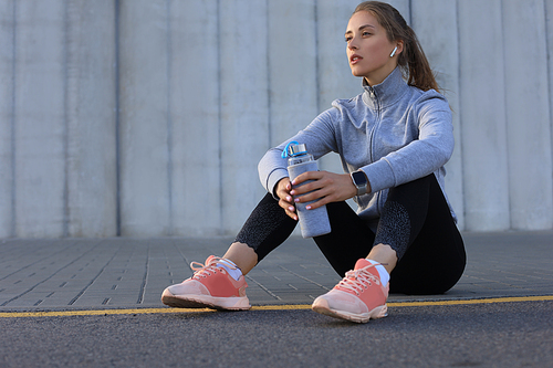 Beautiful young woman in sports clothing drinking water after sport exercise outdoors.