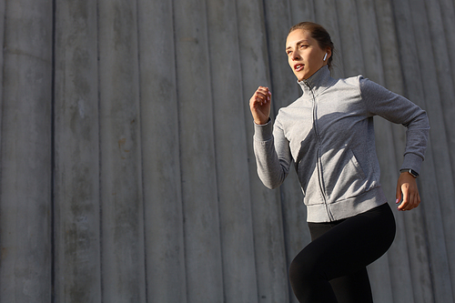 Young attractive sporty fitness woman running while exercising outdoors at sunset or sunrise in city.