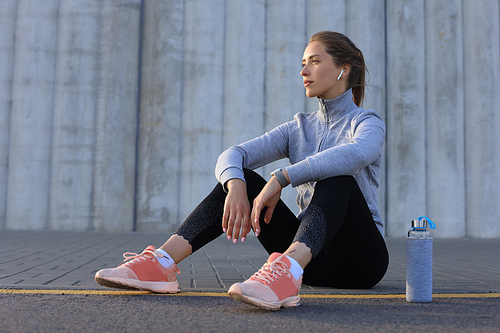 Beautiful young woman in sports clothing drinking water after sport exercise outdoors.