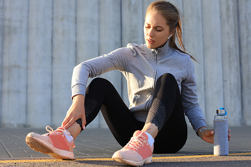 Beautiful young woman in sports clothing drinking water after sport exercise outdoors.