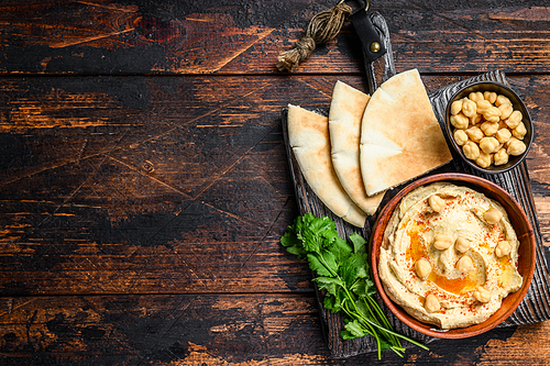 Hummus paste with pita bread, chickpea and parsley in a wooden bowl. Dark wooden background. Top view. Copy space.