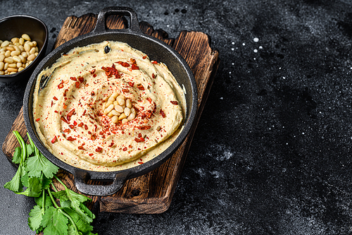 Hummus paste with chickpea and parsley in a bowl. Black background. Top view. Copy space.