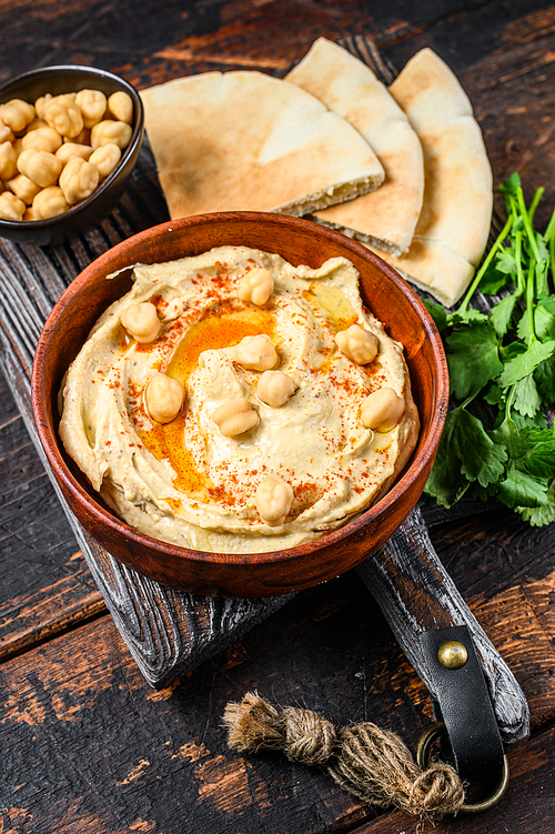 Hummus paste with pita bread, chickpea and parsley in a wooden bowl. Dark wooden background. Top view.