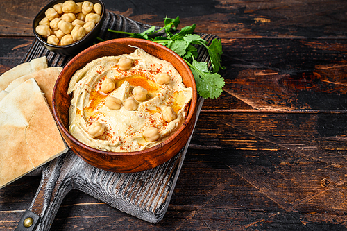 Hummus paste with pita bread, chickpea and parsley in a wooden bowl. Dark wooden background. Top view. Copy space.