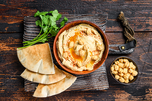 Hummus paste with pita bread, chickpea and parsley in a wooden bowl. Dark wooden background. Top view.