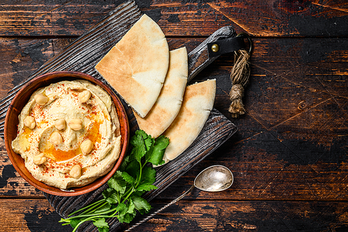 Hummus paste with pita bread, chickpea and parsley in a wooden bowl. Dark wooden background. Top view. Copy space.