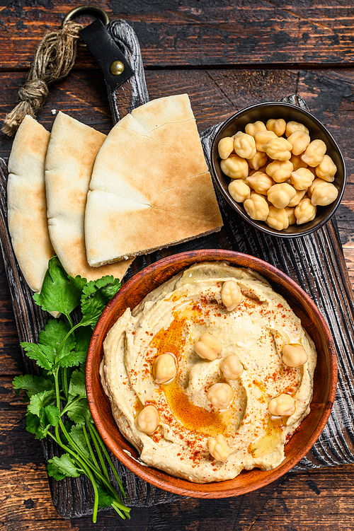 Hummus paste with pita bread, chickpea and parsley in a wooden bowl. Dark wooden background. Top view.