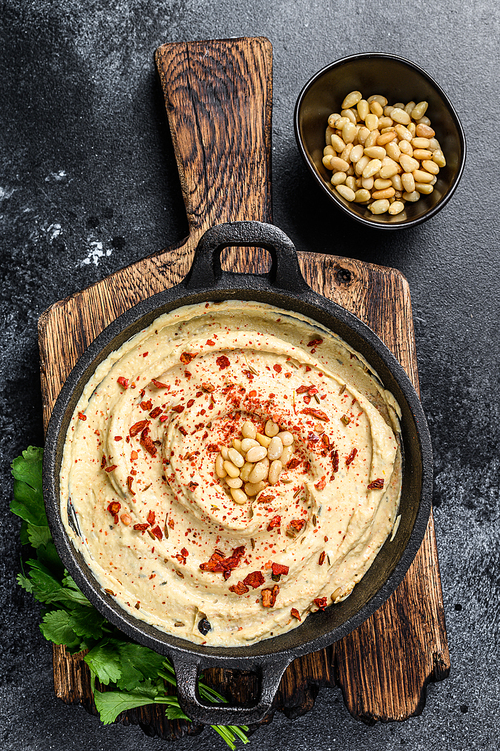 Hummus paste with chickpea and parsley in a bowl. Black background. Top view.