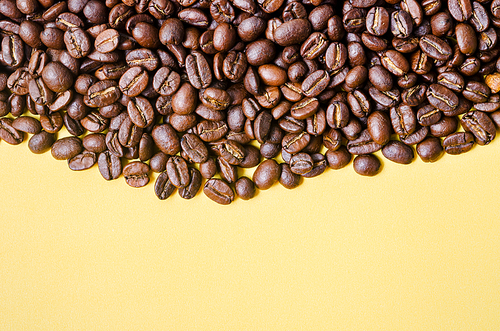 Roasted coffee beans on yellow background with copy space for your text or message.