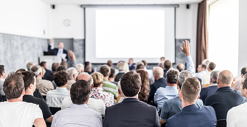 I have a question. Group of business people sitting at the chairs in conference hall. Businessman raising his arm. Conference and Presentation. Business and Entrepreneurship.