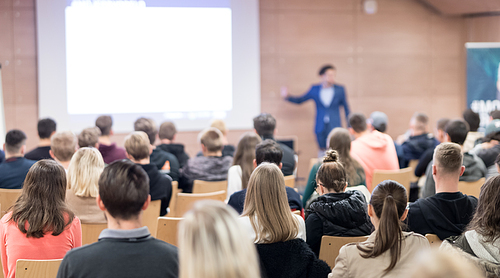 Speaker giving a talk in conference hall at business event. Audience at the conference hall. Business and Entrepreneurship concept. Focus on unrecognizable people in audience.