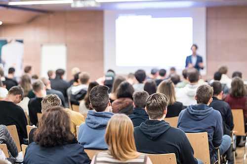 Speaker giving a talk in conference hall at business event. Audience at the conference hall. Business and Entrepreneurship concept. Focus on unrecognizable people in audience.