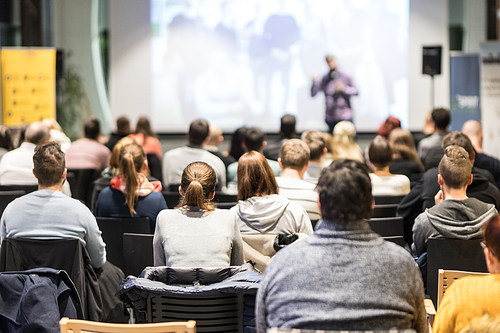 Speaker giving a talk in conference hall at business event. Audience at the conference hall. Business and Entrepreneurship concept. Focus on unrecognizable people in audience.