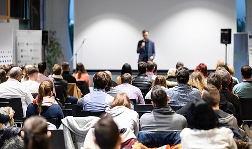 Speaker giving a talk in conference hall at business event. Audience at the conference hall. Business and Entrepreneurship concept. Focus on unrecognizable people in audience.