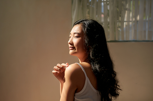 Portrait of beauty smiling asian woman applying a lotion to her arm skin during her morning routine
