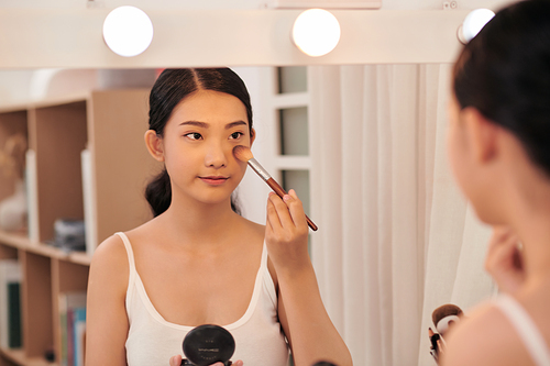 A beautiful young woman sitting at a makeup table and doing her makeup