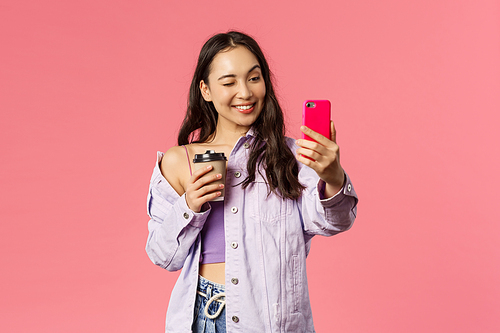 Start your day right. Portrait of good-looking enthusiastic young asian girl in stylish outfit, taking selfie with take-away coffee, recommend followers great cafe to grab drink, pink background.