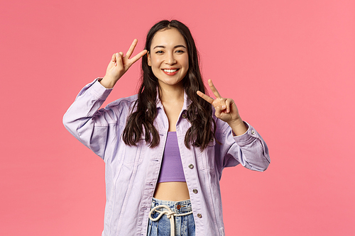 Kawaii asian girl sending good positive vibes, enjoying bright sunny weekend, having fun, partying and brighten up your day with beaming happy smile show peace gesture, pink background.