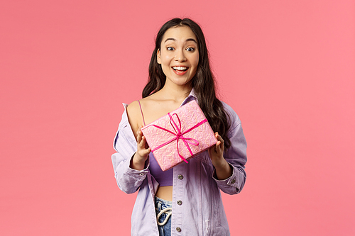 Got present for you. Excited happy young asian girl holding wrapped box with gift, congratulating with holiday or birthday, being invited b-day party, standing amused pink background.