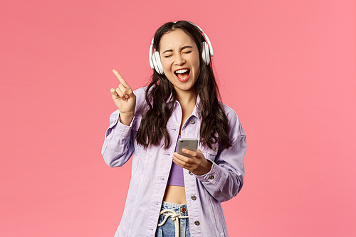 Waist-up portrait of excited and carefree stylish woman enjoying favourite songs, listening music in headphones, close eyes dancing to rhythm and singing along, hold smartphone.
