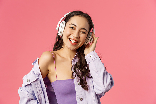 Close-up portrait of charismatic good-looking korean girl enjoying listening music, wear headphones smiling and dancing, found great playlist for walking on fine spring day, pink background.