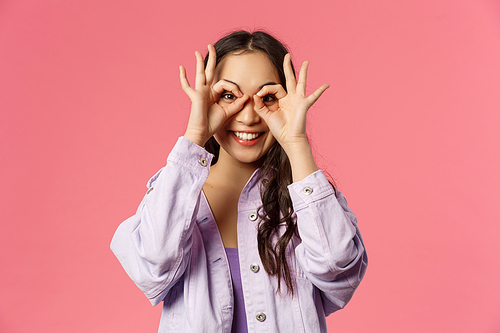 Close-up portrait of charismatic, funny and cute carefree teenage asian girl, making mask with fingers over eyes, smiling and looking camera, having fun, fool around and playing cheerful.
