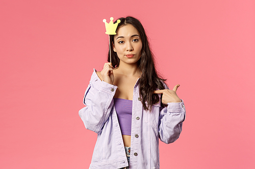 Holidays, lifestyle and people concept. Portrait of confident, sassy young asian woman pointing herself, feeling assertive being a top, hold queen crown stick, pink background.