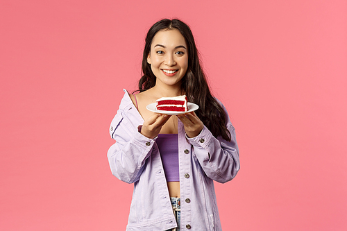 Got you some sweet dessert. Portrait of cheerful young asian girl holding piece of delicious cake, smiling happy, eating out at favorite cafe, standing pink background joyful.