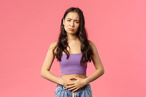 Health, medicine and people concept. Young stylish girl dressed-up for party but started feel pain in stomach, stomachache or menstrual cramps, gloomy looking camera as complaining, pink background.