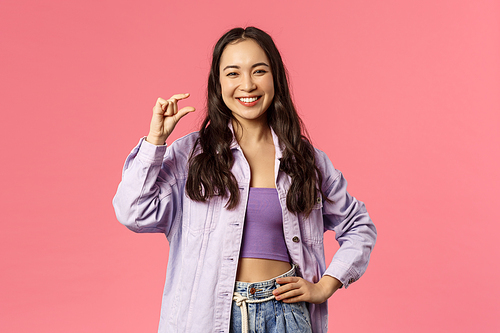 Little effort but big profit. Portrait of cheerful, attractive and carefree modern girl in denim jacket over crop-top, show something is small or tiny, laughing pleased smiling, pink background.