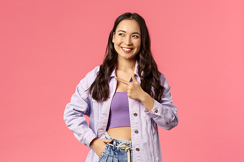 Spring, fashion and lifestyle concept. Confident stylish young asian woman in outfit, pointing finger left and looking at something with pleased smile, found great product, pink background.